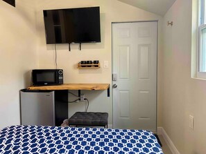 Una camera da letto con un letto, una TV a muro, un forno a microonde e un piccolo ripiano in legno.