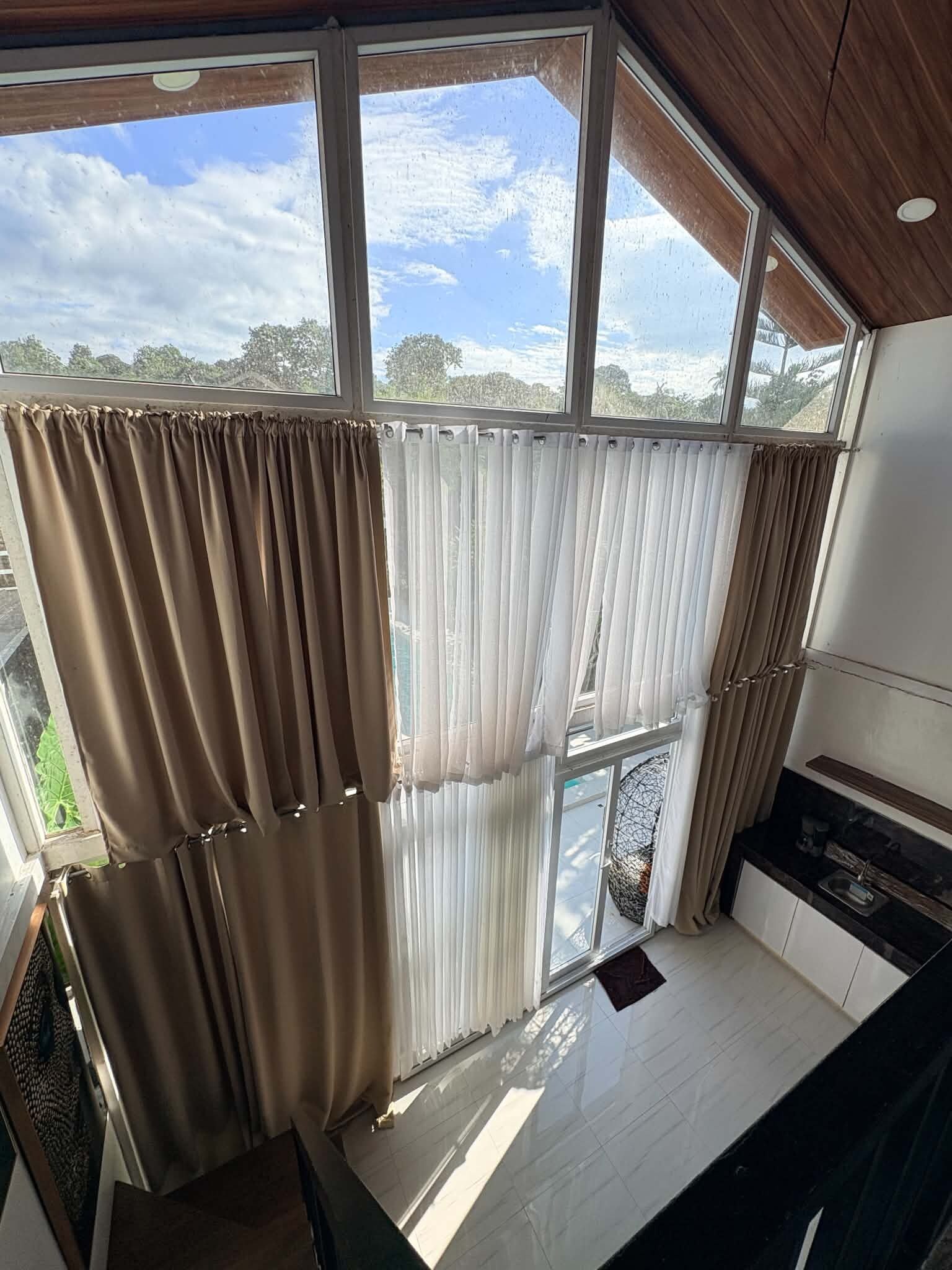 A room with a large window, a kitchen area, and a view of trees and sky.
