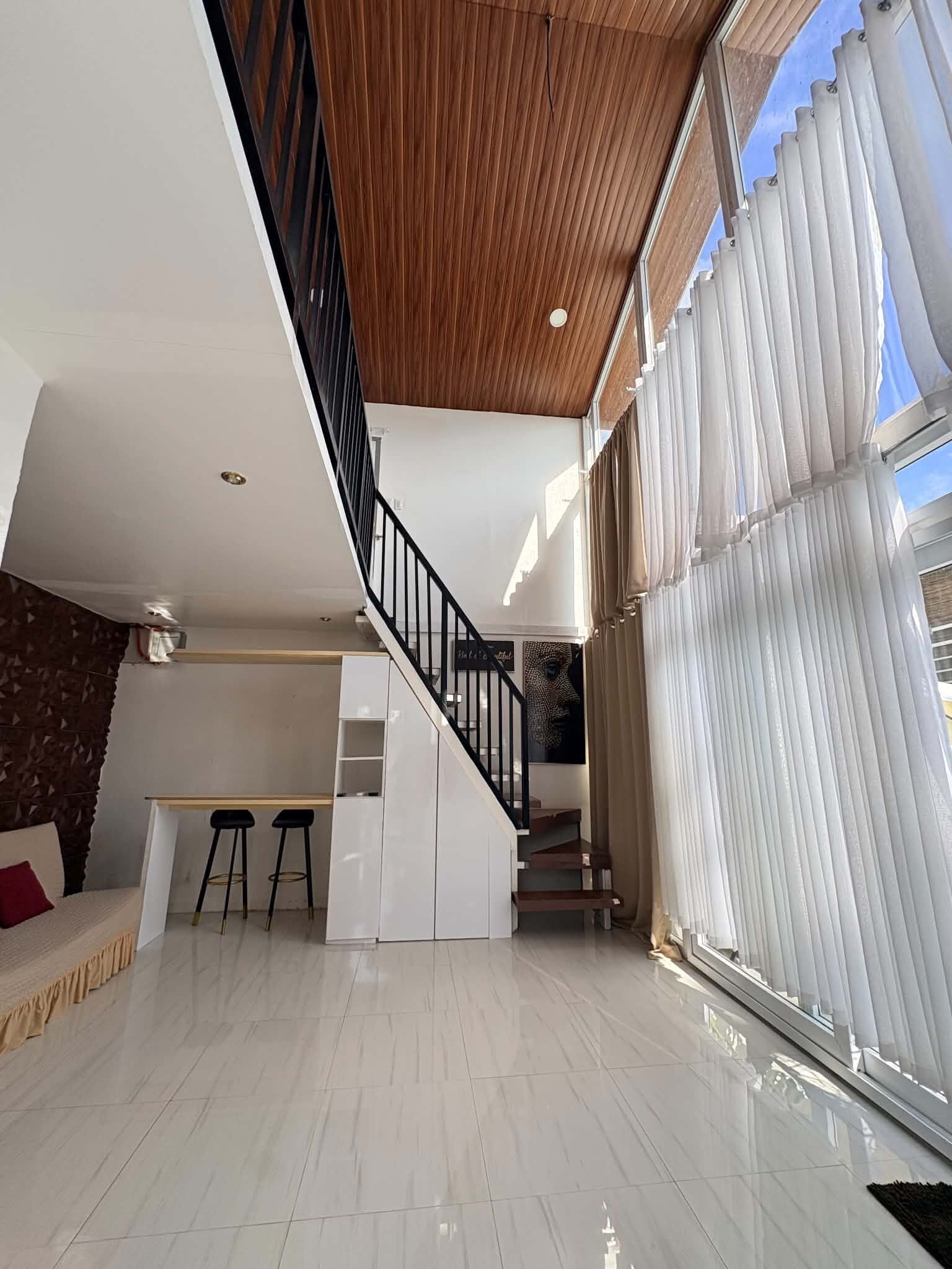 A modern interior with a staircase, a kitchen area, and a large window with blinds.
