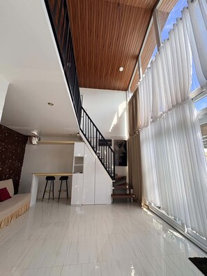 Un intérieur moderne avec un escalier, un coin cuisine et une grande fenêtre équipée de stores.