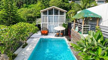 Una piscina con superficie de agua azul cristalina, rodeada de exuberante vegetación y un pequeño edificio con techo de paja.