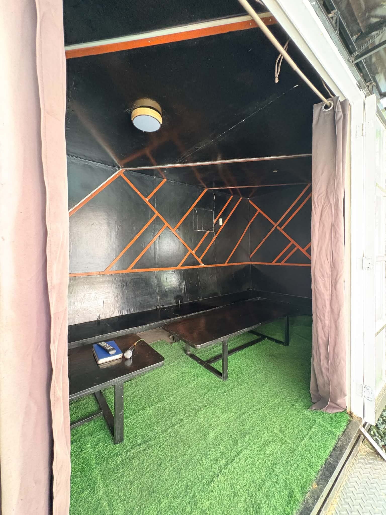 A room with a green artificial turf floor, a table with a remote control and a book, and a bench with a metal frame.