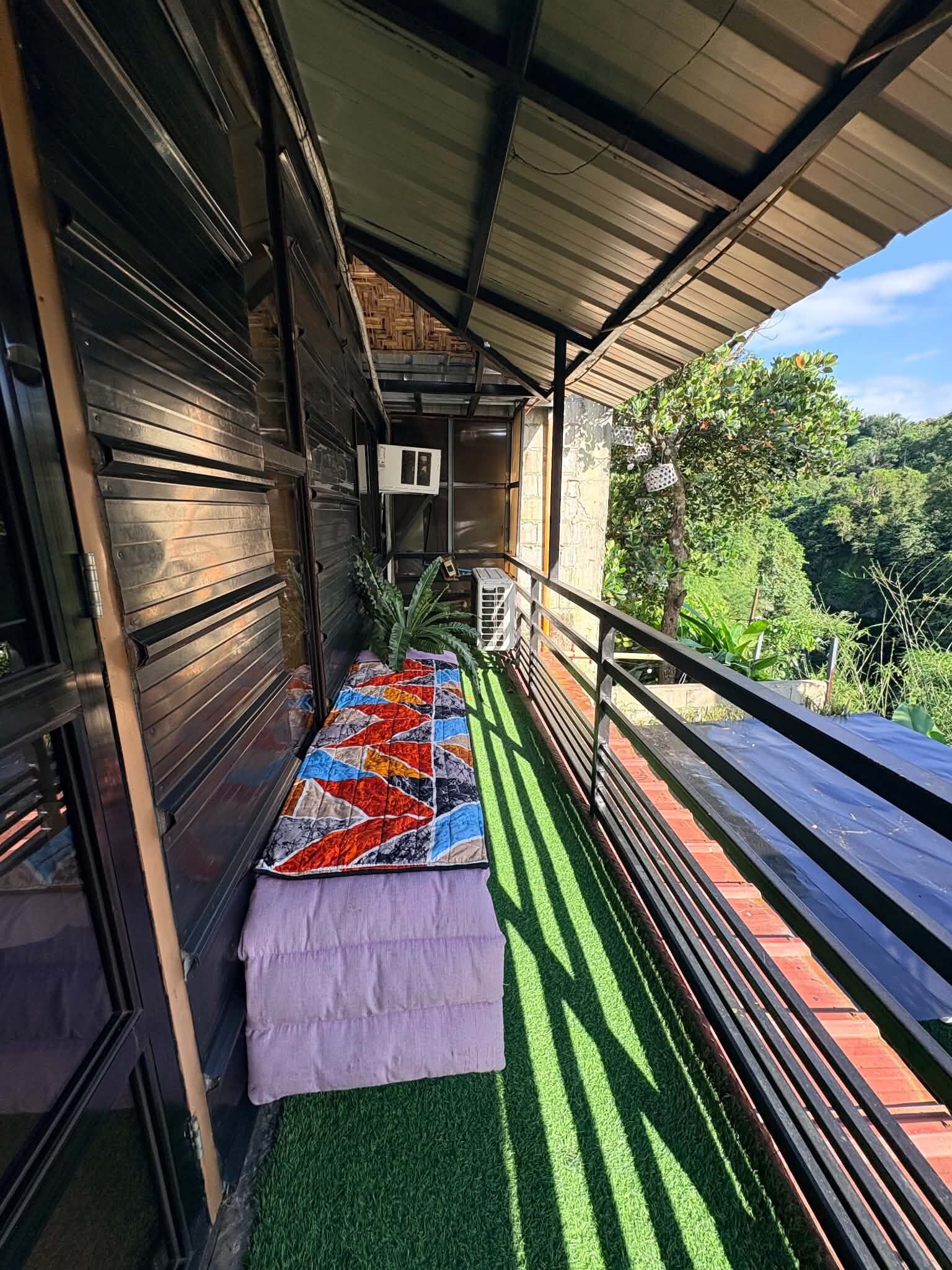 A balcony with a colorful quilt, a small table, and a potted plant.