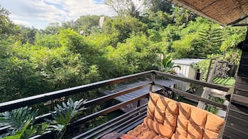 A covered outdoor seating area with a table and chairs, surrounded by lush greenery and a view of the landscape.