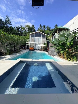 A swimming pool with a clear view of the surrounding area, including a building with a white facade and a tropical garden. - Green Villa Private Resort Tropical Luxury, Private Pool & Nature Escape (Cavite)