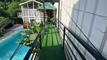 A pool area with a clear view of the sky, a white building, and lush greenery.