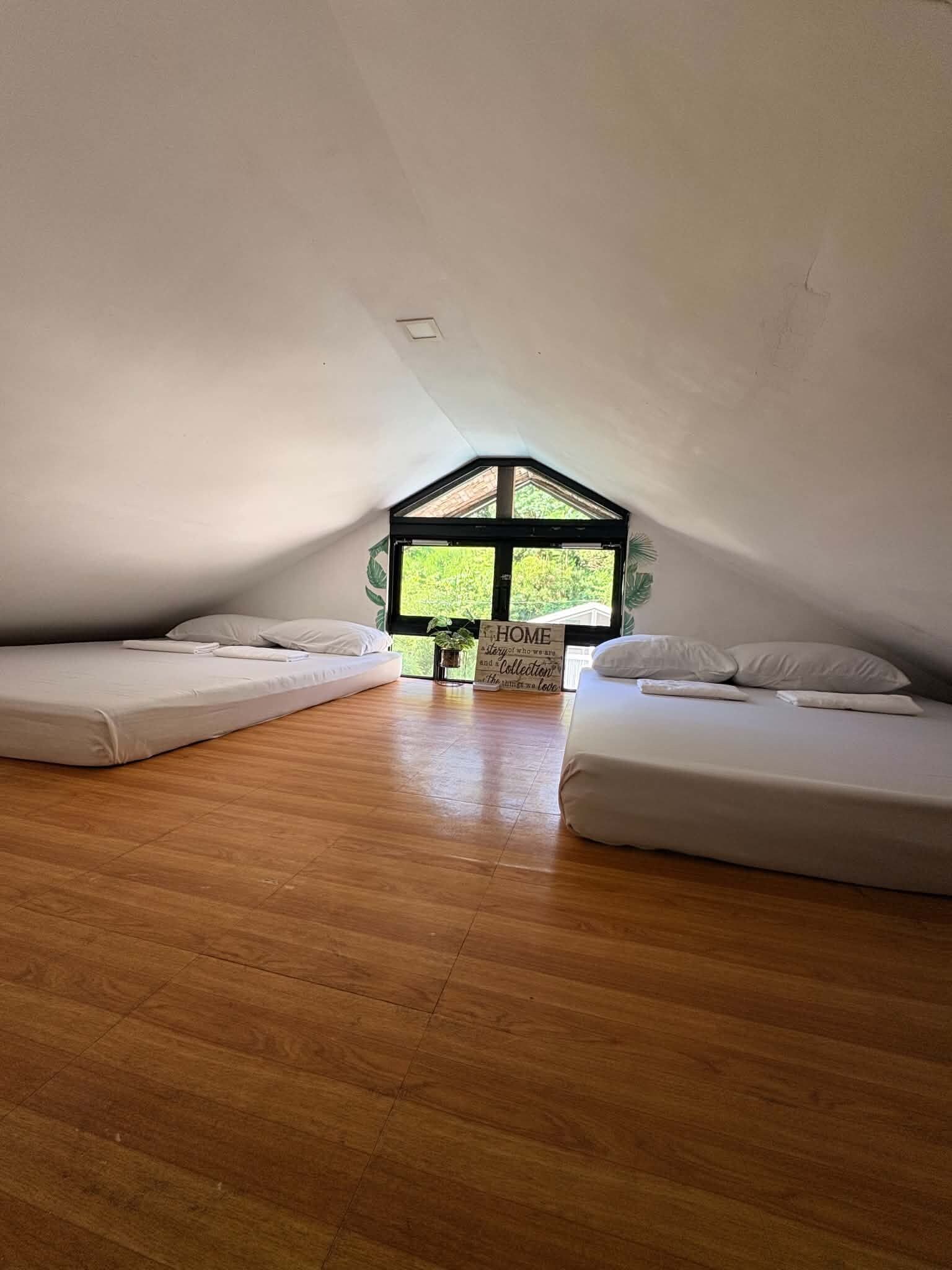 A small, triangular attic room with two beds and a large window.