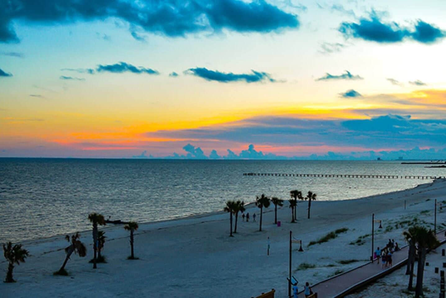 Une plage avec une jetée qui s’avance dans l’eau, des palmiers et un ciel dégagé.