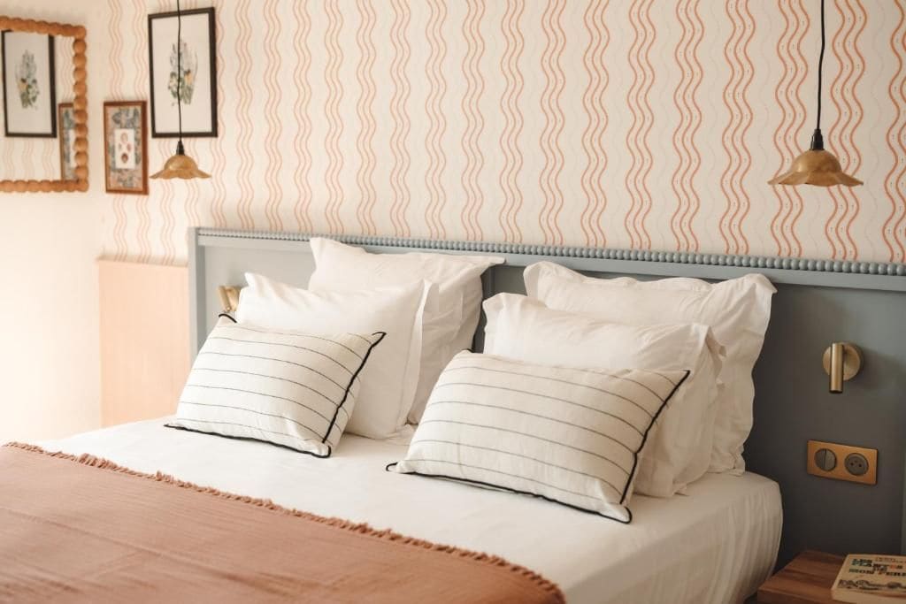 A neatly made bed with a striped pillow, a headboard, and a wall with a wavy pattern.