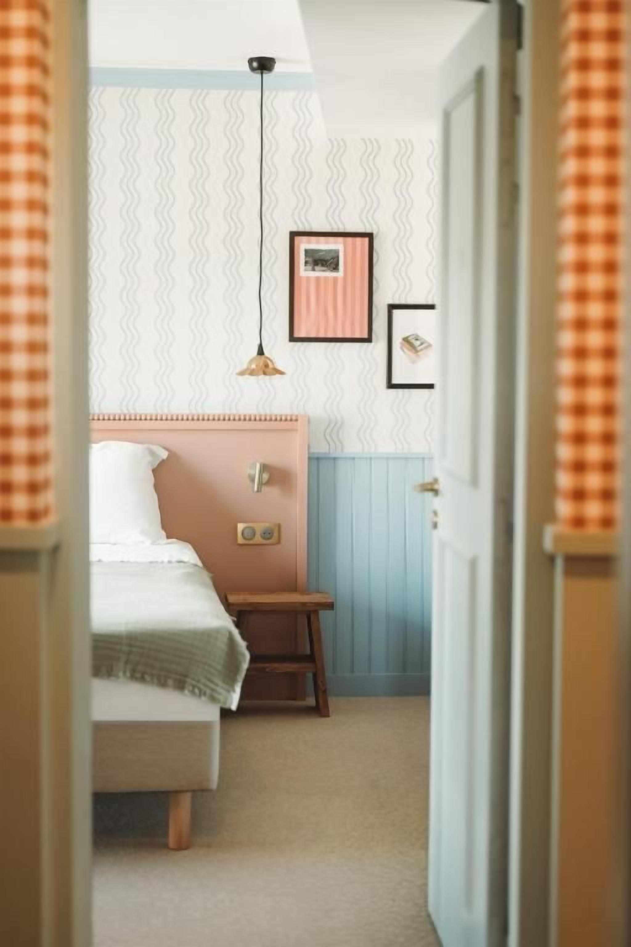 Un dormitorio con una cama, una mesita de noche, una lámpara colgante y un cuadro en la pared.