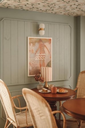 A dining area with a wooden table, wicker chairs, a wall-mounted light fixture, and a framed picture above the table. - HOTEL SAINT-ENOGAT (Dinard)