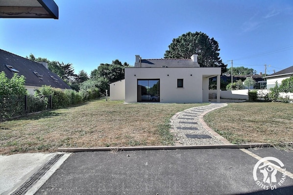 A modern building with a flat roof, a large glass door, and a paved driveway leading to the entrance. - The Temple of Happiness (PLENEUF VAL ANDRE)