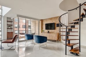 A modern living room with a spiral staircase, large windows, and a flat-screen TV mounted on a brick wall. - New Listing (Bogotá)