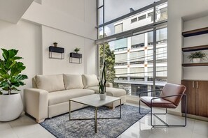 A modern living room with a sofa, coffee table, and chair, large windows, and potted plants. - New Listing (Bogotá)