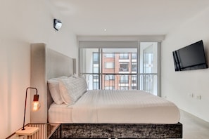 A modern bedroom with a large bed, a TV mounted on the wall, and a balcony with a city view. - New Listing (Bogotá)