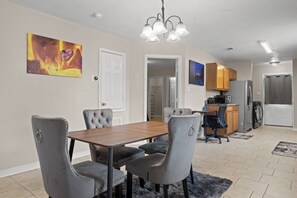 A dining area with a wooden table and grey upholstered chairs, a kitchen with wooden cabinets, and a grey rug on the floor. - Aladdin Themed Condo Near Base and the Beach (Biloxi)