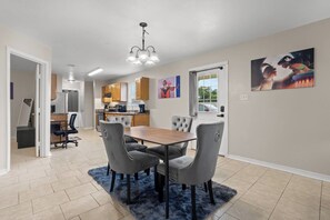 A modern kitchen with wooden cabinets, a dining area with a wooden table and grey upholstered chairs, and artwork on the walls. - Aladdin Themed Condo Near Base and the Beach (Biloxi)