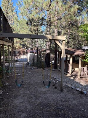 A wooden swing set in a wooded area with a covered seating area and a building in the background. - Enjoy an Escape at Big Bear Lake (Big Bear Lake)