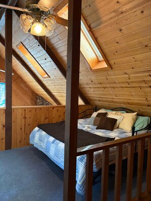 Een slaapkamer met een schuine kap, een bed met metalen frame en een houten vloer.