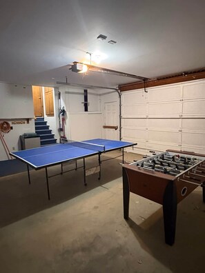 Een kamer met een tafeltennistafel, een tafelvoetbaltafel, een trap en een garagedeur.