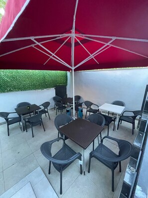 An outdoor patio area with a red umbrella, multiple tables and chairs, and a grill. - KADIKÖY MERKEZDE (İstanbul)