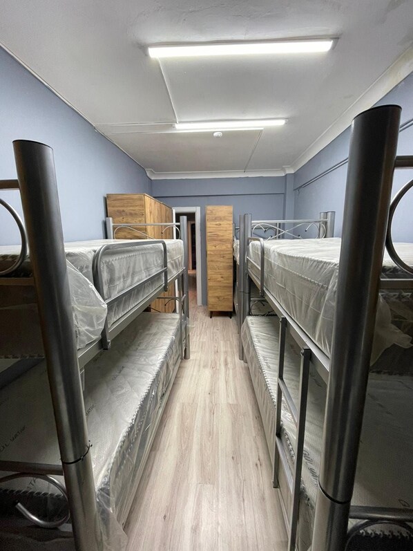 Quarto em dormitório com beliches, guarda-roupa de madeira e luminária no teto.