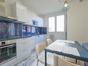 A modern kitchen with white cabinets, a Bosch oven, and a dining area with a table and chairs. - New Listing (Paris)