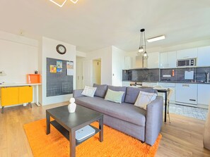 A modern apartment with a grey sofa, a small table, and a kitchen area with white cabinets and a black backsplash. - New Listing (Paris)
