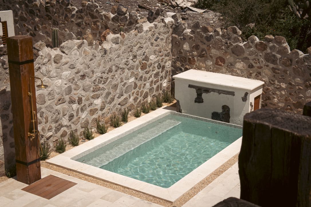 Una piscina rectangular con agua cristalina, rodeada por un muro de piedra y una terraza de madera.