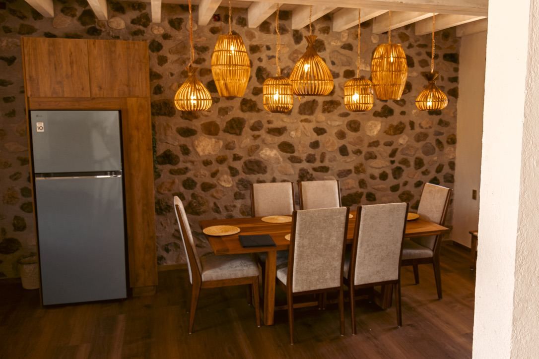Cocina con refrigerador, mesa de comedor, sillas y lámparas colgantes.