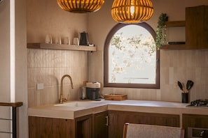 Una cocina con un armario de madera, un lavamanos, un ventanal y una lámpara colgante.