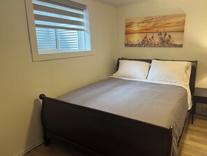 Ein Schlafzimmer mit einem Bett, einem Fenster mit Jalousien und einem Gemälde an der Wand.