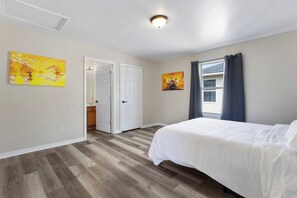 Une chambre à coucher avec un lit, une porte donnant sur une salle de bain et deux tableaux accrochés au mur.
