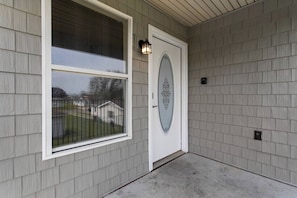 Une façade de maison avec une porte blanche, une fenêtre ornée d’une grille métallique et un luminaire placé au-dessus de la porte.