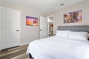 A bedroom with a large bed, two doors, and two wall-mounted paintings. - Dreamworks Themed Beach Escape (Biloxi)