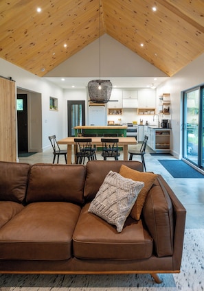Een moderne woonkamer met een bruine leren bank, een eettafel en een keuken op de achtergrond.