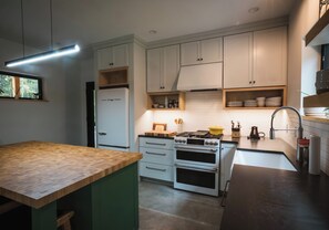 A modern kitchen with white cabinets, a built-in oven, and a wooden countertop. - NEW Cozy home located within minutes to Sugarloaf (Carrabassett Valley)
