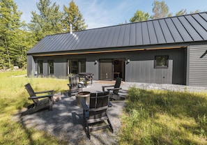 A modern house with a metal roof, a patio with outdoor furniture, and a fire pit. - NEW Cozy home located within minutes to Sugarloaf (Carrabassett Valley)
