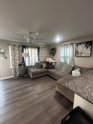 A living room with a sectional sofa, a small side table, and a ceiling fan.