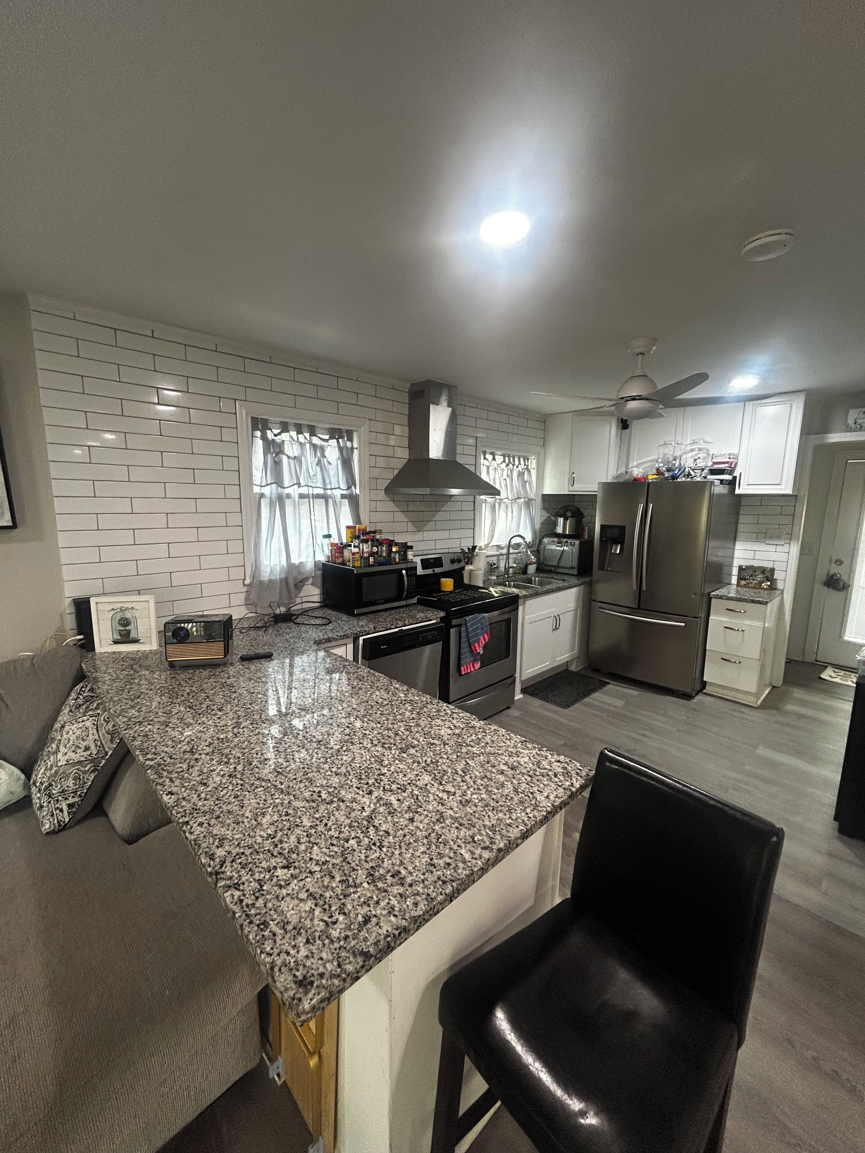 A modern kitchen with granite countertops, stainless steel appliances, and a black leather chair.
