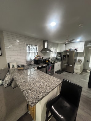 A modern kitchen with granite countertops, stainless steel appliances, and a black leather chair.