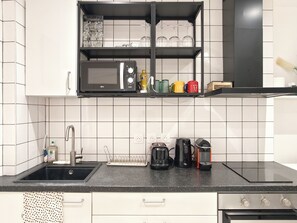 A kitchen with a black countertop, a sink, a coffee maker, a kettle, and a microwave. - New Listing (Paris)