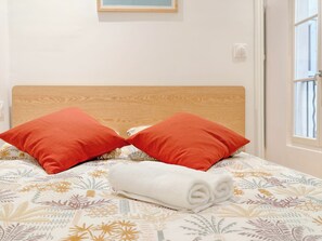 A bed with a wooden headboard, two red pillows, and a rolled white towel. - New Listing (Paris)