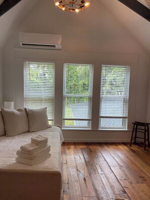 A bedroom with a bed, a stack of towels, a nightstand, and a wooden floor.