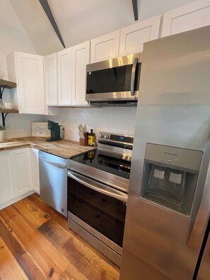 A modern kitchen with white cabinetry, stainless steel appliances, and a wooden countertop.