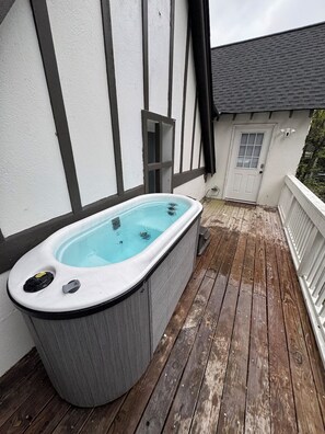 A hot tub on a wooden deck with a white building in the background.