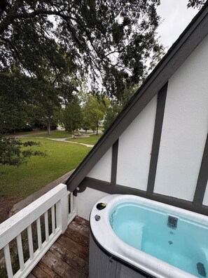 A hot tub on a wooden deck with a white and dark trim wall, overlooking a grassy yard with trees.