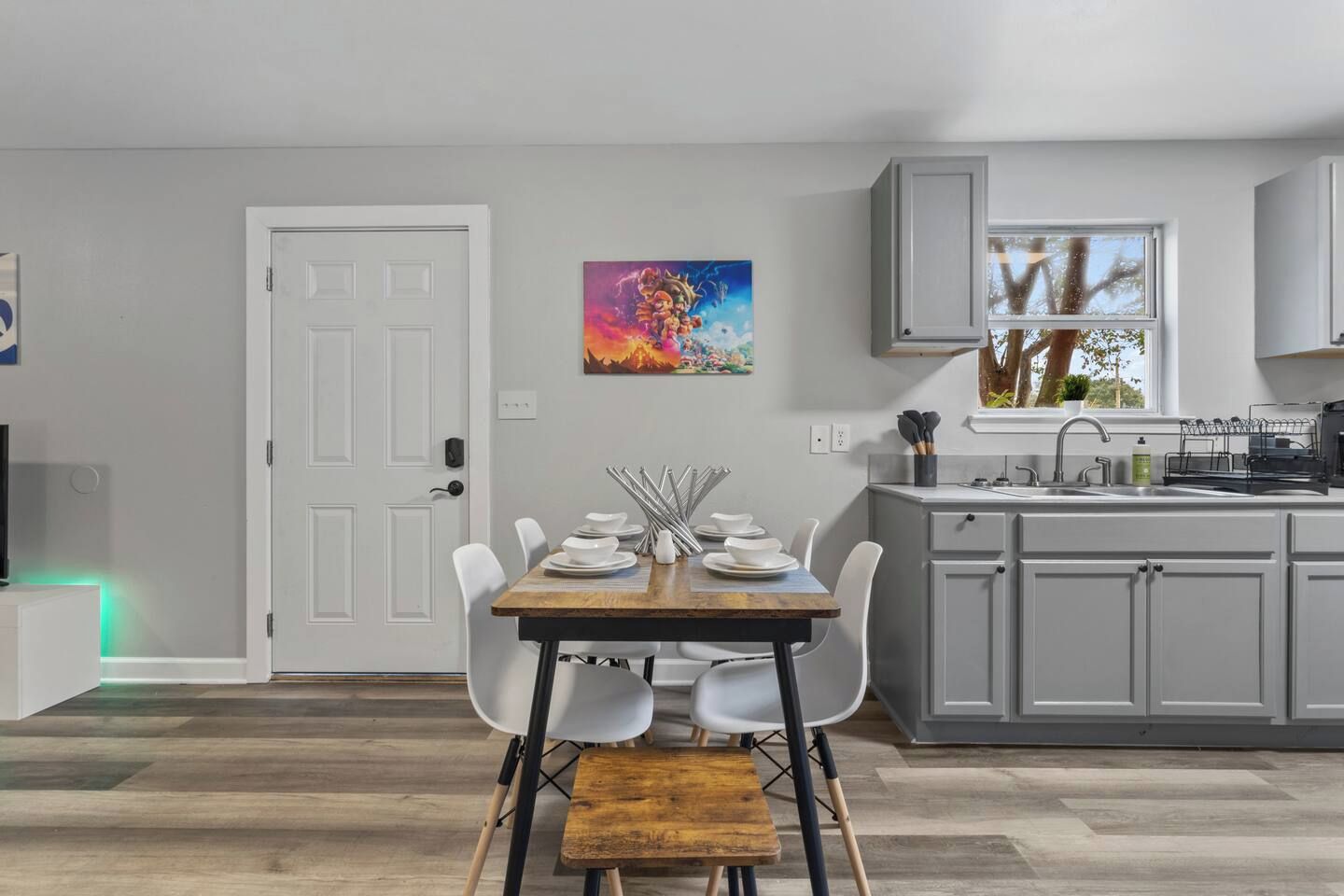 A modern kitchen with a dining area, featuring a wooden table, white chairs, and a painting on the wall.