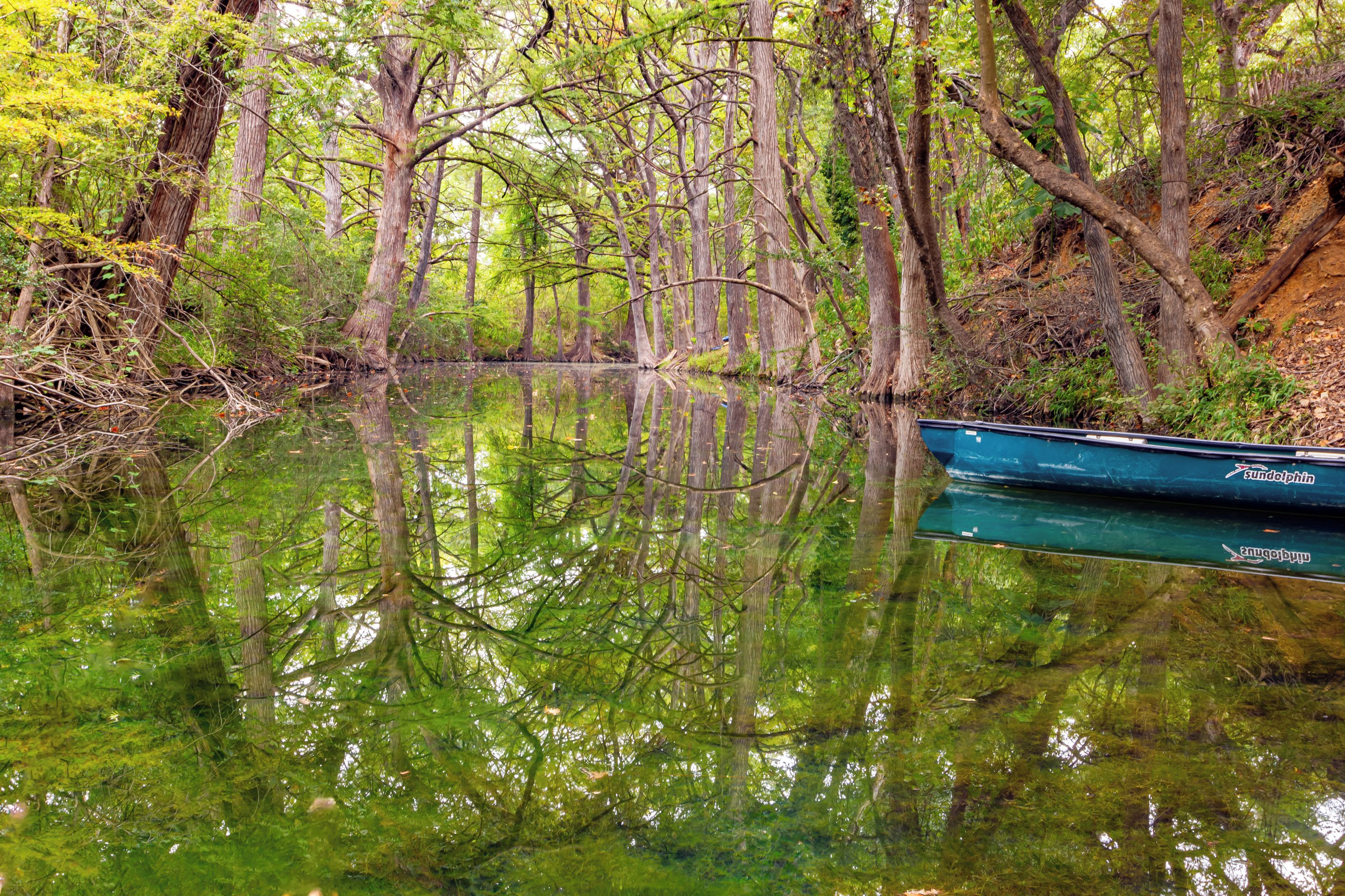 A calm river with dense trees and a boat docked on the right.