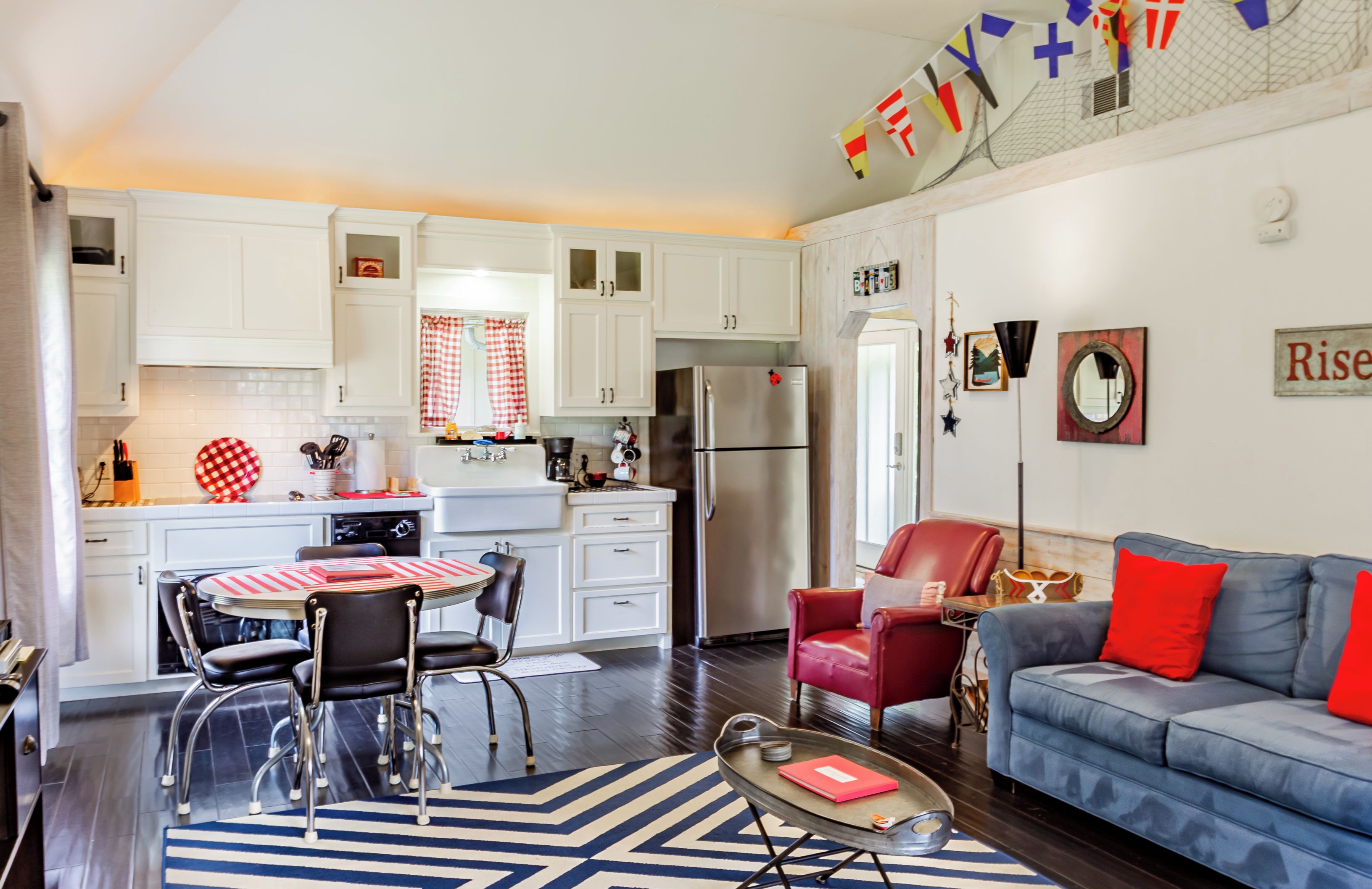 A modern kitchen with white cabinets, a stainless steel refrigerator, and a dining area with a red and white checkered tablecloth.